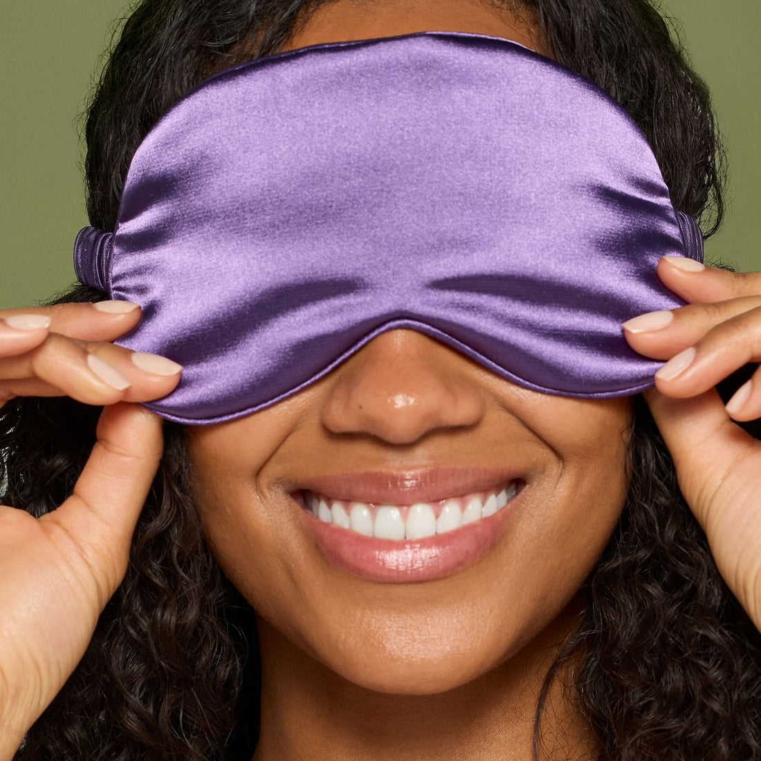 A woman smiling with the satin sleep mask from the Jane Iredale Well Rested kit over her eyes
